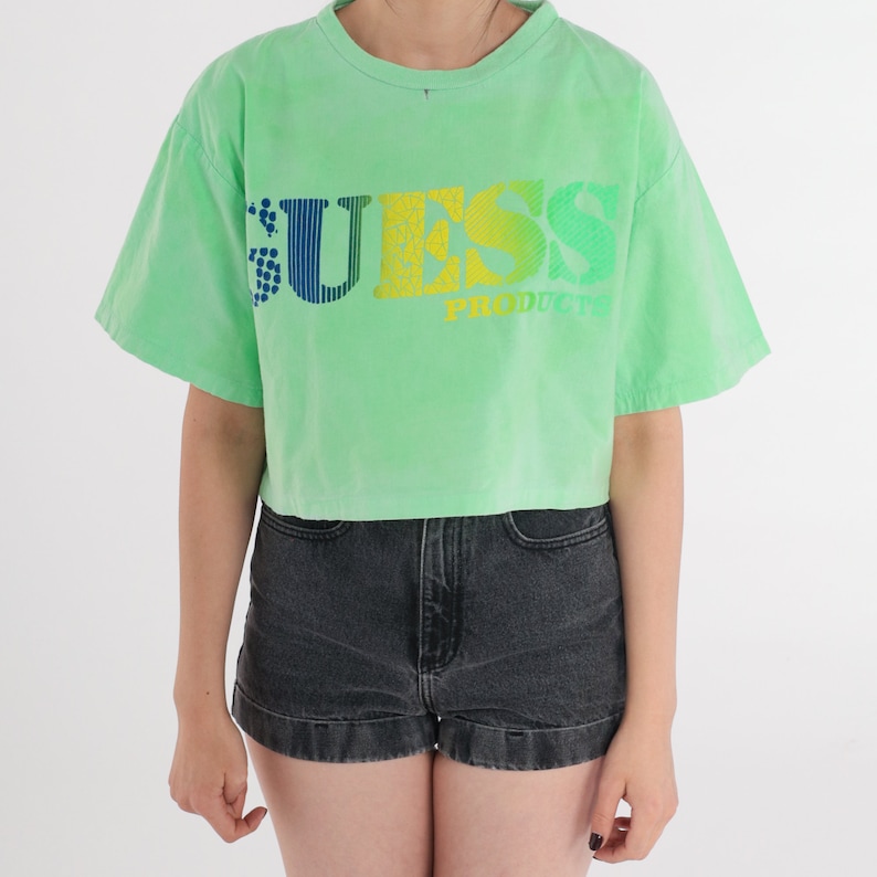 May include: A green cropped t-shirt with a rainbow coloured "GUESS PRODUCTS" logo.