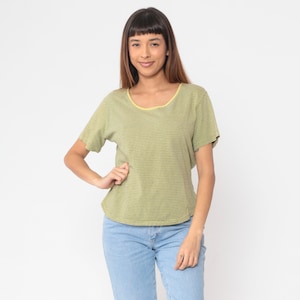 Peut inclure: Un t-shirt &agrave; rayures vert clair avec un col jaune. Le t-shirt &agrave; manches courtes est associ&eacute; &agrave; un jean bleu clair. Le mod&egrave;le pose une main sur la hanche.