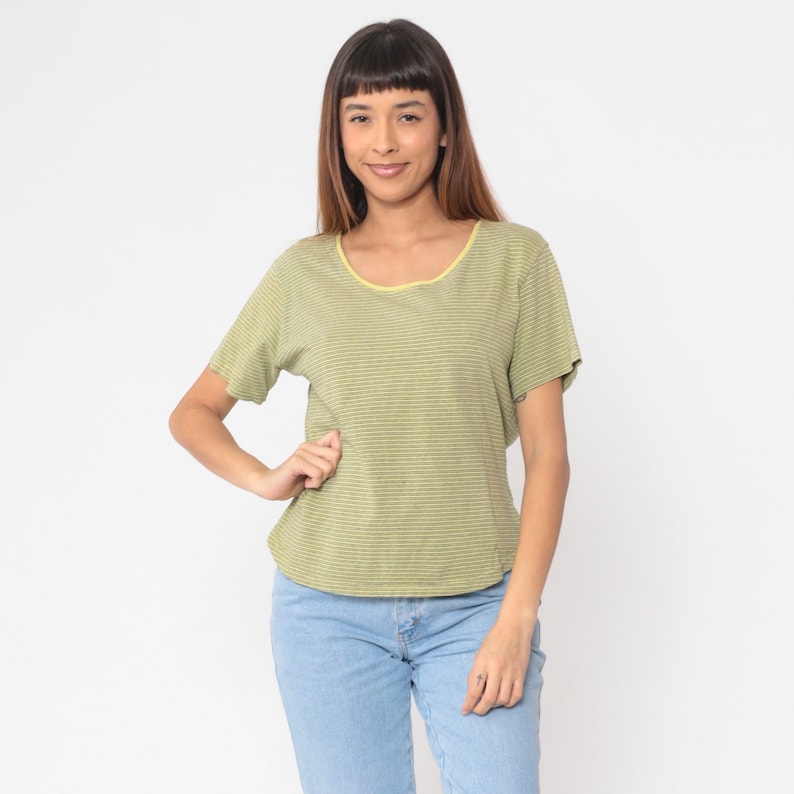 Peut inclure: Un t-shirt &agrave; rayures vert clair avec un col jaune. Le t-shirt &agrave; manches courtes est associ&eacute; &agrave; un jean bleu clair. Le mod&egrave;le pose une main sur la hanche.