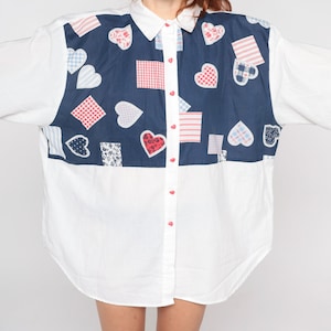 May include: A white button-down shirt with a blue panel featuring a patchwork design of red, white and blue hearts and squares.