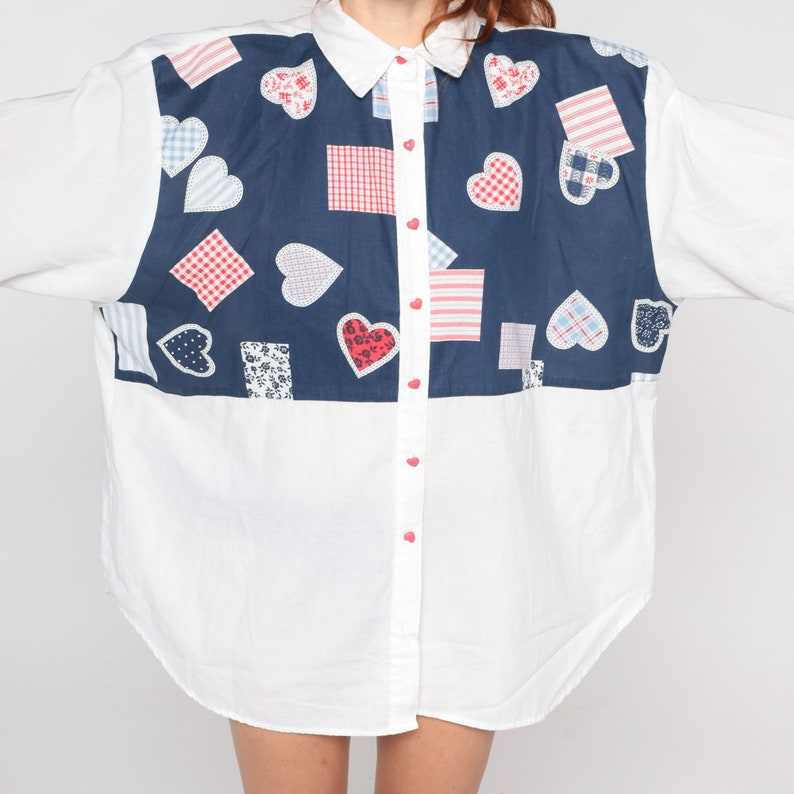 May include: A white button-down shirt with a blue panel featuring a patchwork design of red, white and blue hearts and squares.
