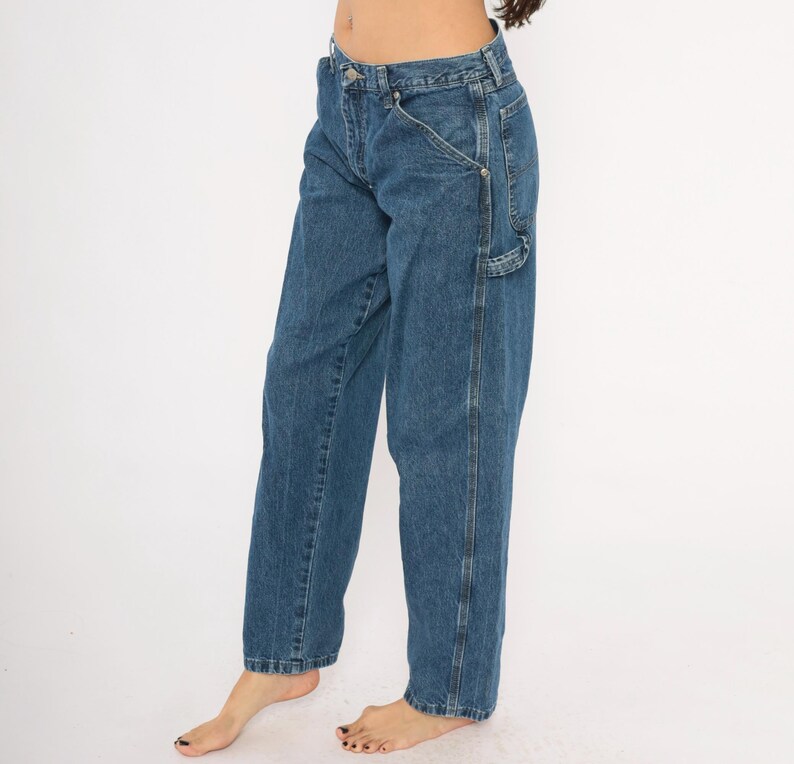 May include: Blue denim carpenter pants with a relaxed fit. The jeans feature a classic five-pocket design, a hammer loop, and a utility pocket. The pants have a straight leg and a medium wash.
