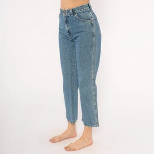May include: Light blue denim jeans with a high waist and straight leg. The jeans have a classic five-pocket design and a button and zipper closure. The jeans are cropped at the ankle.
