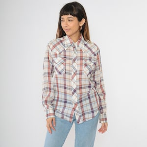 May include: A long-sleeved plaid shirt with a white background and red, blue, and purple plaid pattern. The shirt has a collared neckline, button closure, and two chest pockets.
