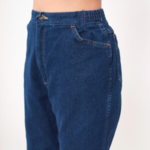 K&ouml;nnte beinhalten: Nahaufnahme einer dunkelblauen Jeanshose. Die Hose hat einen Knopf und einen elastischen Bund. Die Vordertasche und die N&auml;hte sind mit orangefarbenen N&auml;hten versehen. Die Hose ist aus robustem Denim-Material.