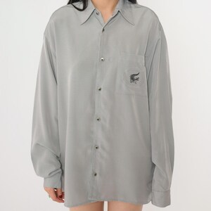 May include: A gray long-sleeved button-down shirt with a small alligator logo embroidered on the left chest pocket.