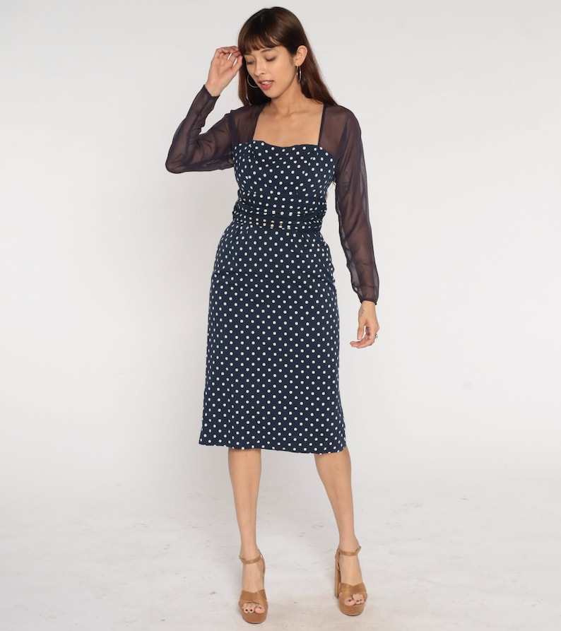 May include: A navy blue midi dress with white polka dots and a sheer black overlay. The dress has a square neckline and a fitted silhouette.