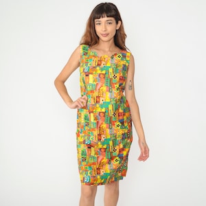 Puede incluir: Un vestido sin mangas, hasta la rodilla, con un vibrante y colorido estampado abstracto. El vestido presenta un escote festoneado y una silueta ajustada. El patrón incluye formas geométricas amarillas, verdes, naranjas y azules.