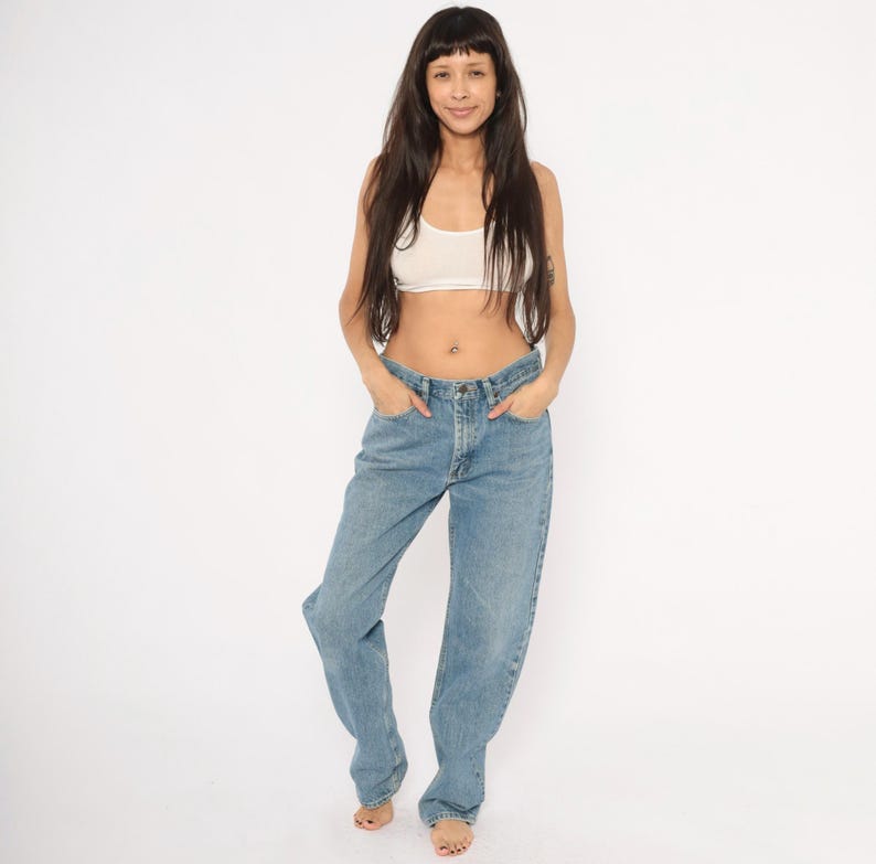 Peut inclure: Une femme porte un haut court blanc et un jean en denim bleu clair. Le jean a une conception classique &agrave; cinq poches et une coupe d&eacute;contract&eacute;e. Le mod&egrave;le se tient devant un fond blanc.