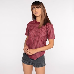 May include: A burgundy striped short-sleeved shirt with a round neckline. The shirt is made of a soft, textured fabric.
