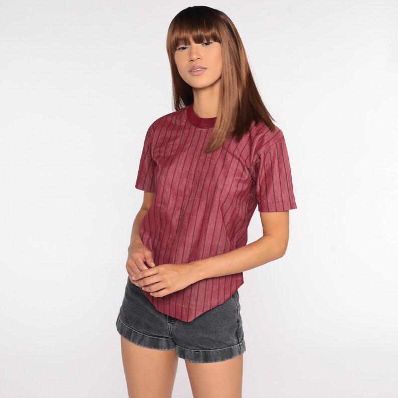 May include: A burgundy striped short-sleeved shirt with a round neckline. The shirt is made of a soft, textured fabric.