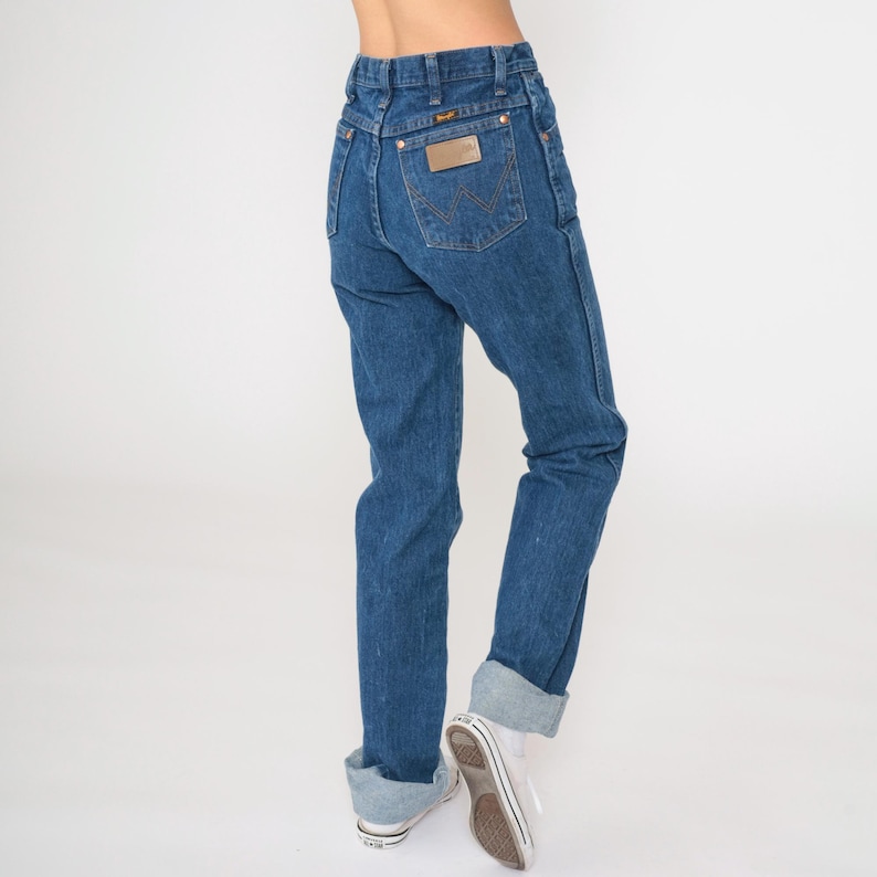 May include: A pair of blue denim jeans with a brown leather patch on the back pocket that says "Wrangler".