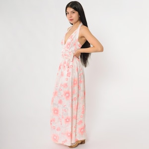 May include: A halter-neck maxi dress with a floral pattern in shades of pink and white. The dress features a deep V-neckline and a gathered waist detail. The long skirt flows to the floor.