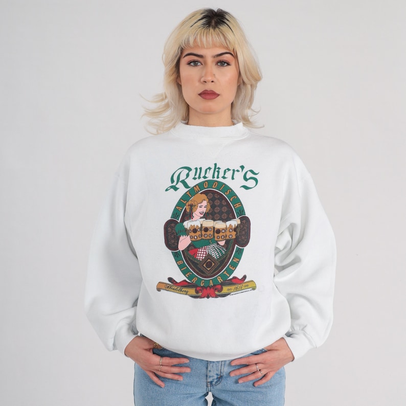 May include: White sweatshirt with a green and gold logo that says "Rucker's Altmo dische Biergarten" and features a woman holding beer steins.