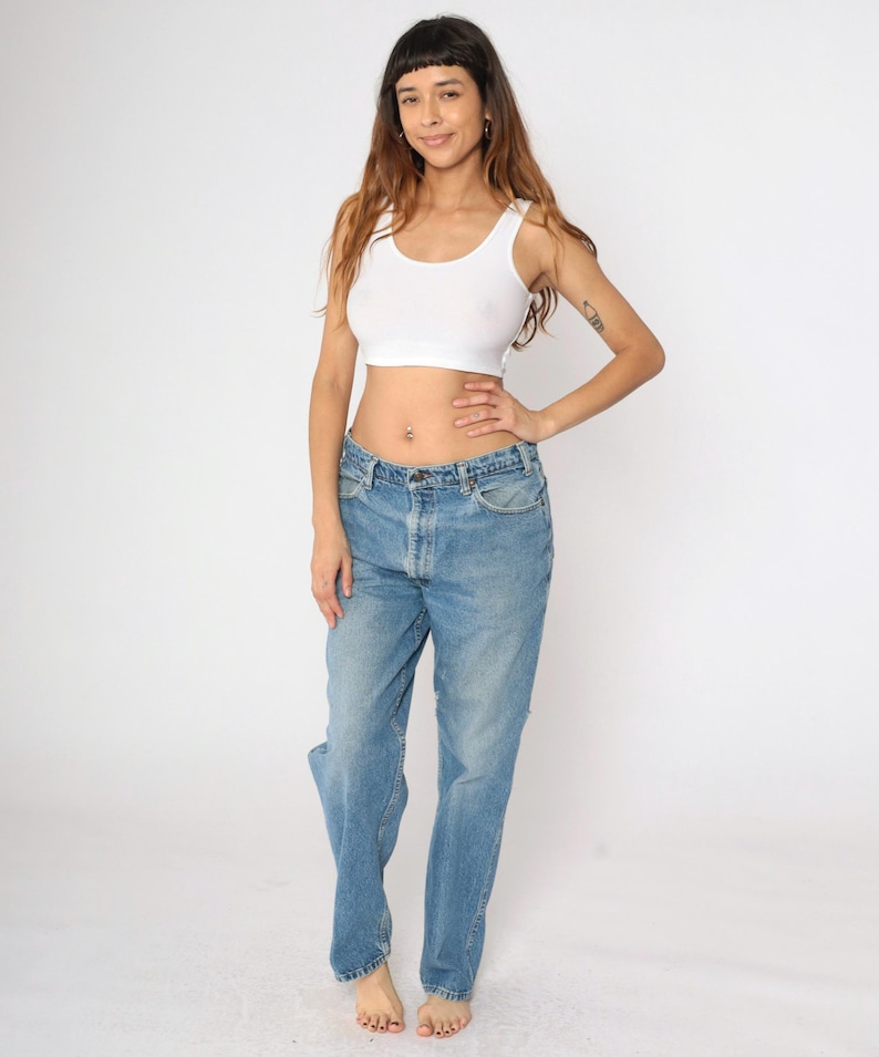 May include: A woman wearing a white crop top and light blue denim jeans. The jeans have a high waist and a straight leg.
