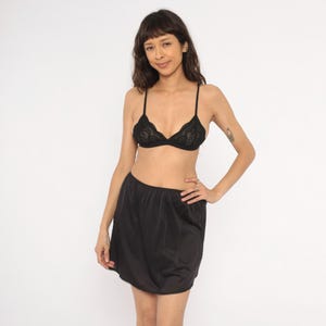 May include: Black lace bra with spaghetti straps and a matching black slip skirt. The bra features a delicate floral lace pattern. The slip skirt is a solid black color and has a simple, classic design.
