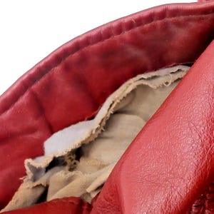 May include: Close-up of a red leather jacket, showing the collar and interior lining. The leather has a textured appearance, with visible wear and tear. The lining is a light beige fabric, partially exposed.