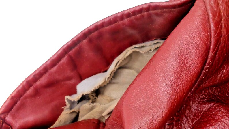 May include: Close-up of a red leather jacket, showing the collar and interior lining. The leather has a textured appearance, with visible wear and tear. The lining is a light beige fabric, partially exposed.