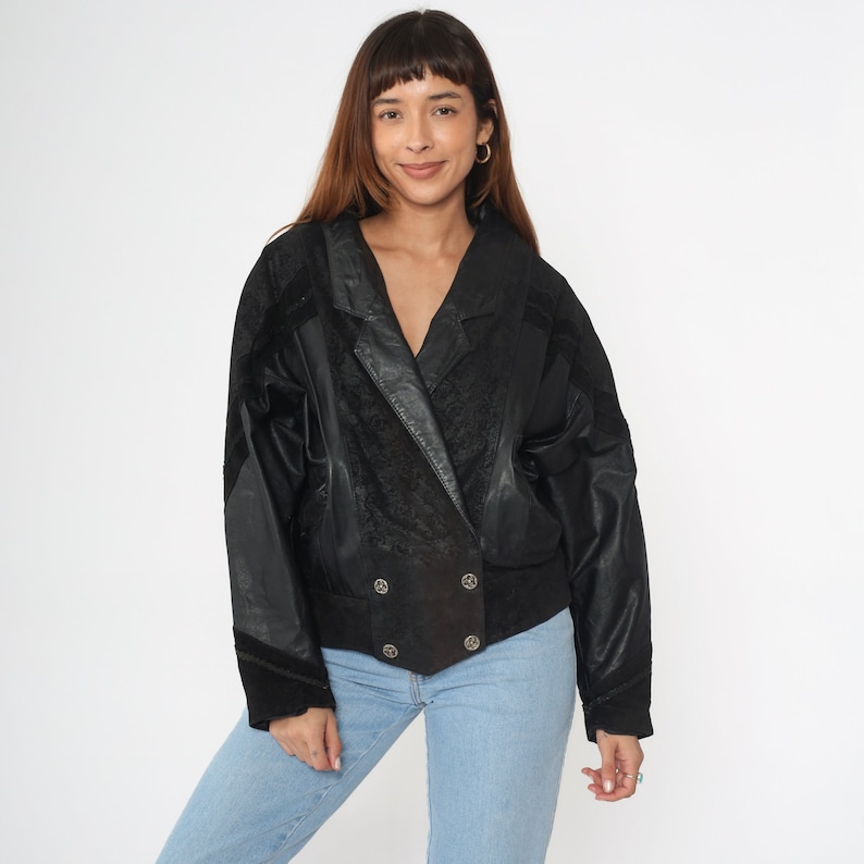 May include: A black leather jacket with a suede collar and double-breasted closure. The jacket has a textured pattern and a slightly cropped fit.