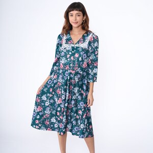 K&ouml;nnte beinhalten: Ein blaues Midi-Kleid mit einem wei&szlig;en Spitzenkragen und einem Blumenmuster. Das Kleid hat einen Knopfleisten vorne und 3/4-&Auml;rmel.