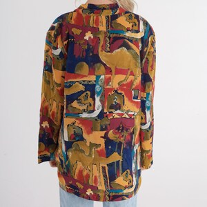 May include: A long-sleeved, oversized blazer with a colorful, patterned design. The pattern features camels, figures, and architectural elements in shades of gold, red, blue, and brown. The blazer has a collared neckline and a loose fit.