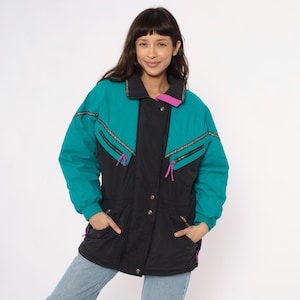 May include: Teal and black winter jacket with a high collar and gold zipper accents. The jacket has a black center panel and teal sleeves. The collar has a pink accent. The jacket has two front pockets and gold buttons.