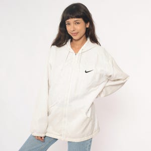 Puede incluir: Chaqueta con capucha color crema con el logo negro de Nike. La chaqueta tiene cierre de cremallera completo y dos bolsillos delanteros. Fabricada con material ligero.