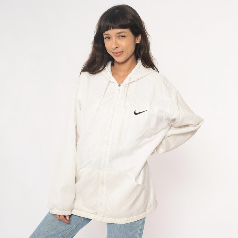 Puede incluir: Chaqueta con capucha color crema con el logo negro de Nike. La chaqueta tiene cierre de cremallera completo y dos bolsillos delanteros. Fabricada con material ligero.