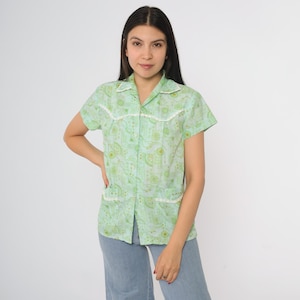 Könnte beinhalten: Ein hellgrünes kurzärmeliges Hemd mit weißer Spitzenborte und einem sich wiederholenden Muster aus grünen Formen. Das Hemd hat zwei Taschen und einen Kragen. Die Person trägt eine hellblaue Jeans.