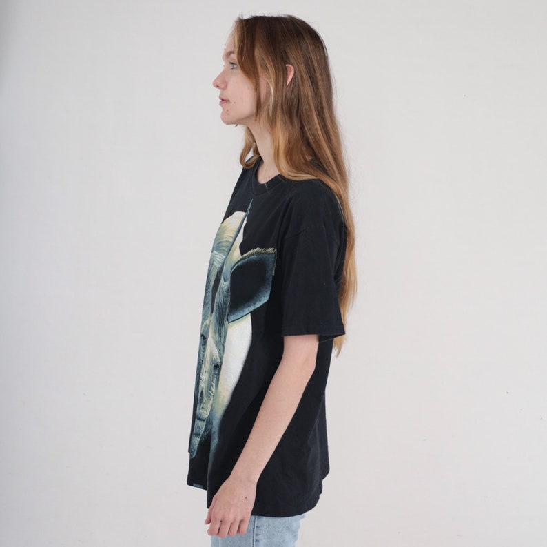 以下が含まれることがあります： 白いサイの頭部のグラフィックプリントが施された黒いTシャツ。クルーネックと半袖です。