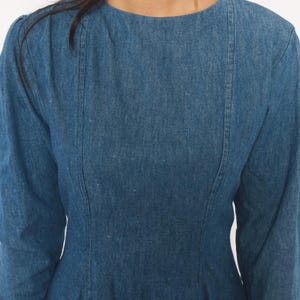 Puede incluir: Un vestido de mezclilla azul de manga larga con cuello redondo y detalles de costuras verticales que van desde los hombros hasta el corpi&ntilde;o, creando un ajuste estructurado en el torso con una textura de tela de lavado medio.