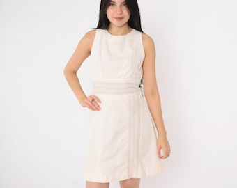 Puede incluir: Un vestido blanco sin mangas con un delicado ribete de encaje en la cintura. El vestido tiene una silueta simple, de línea A y una falda ligeramente acampanada.