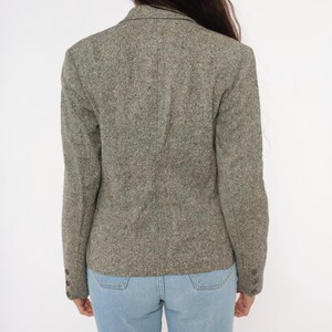 May include: A gray tweed blazer with a notched lapel and buttoned cuffs. The blazer has a classic, tailored fit and is made of a textured fabric. The blazer is paired with light blue jeans.