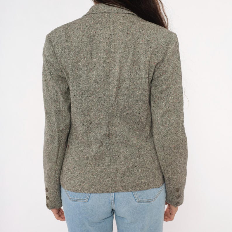 May include: A gray tweed blazer with a notched lapel and buttoned cuffs. The blazer has a classic, tailored fit and is made of a textured fabric. The blazer is paired with light blue jeans.