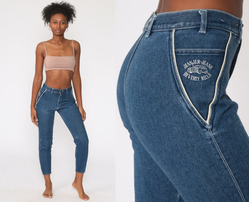 Puede incluir: Vaqueros de mezclilla azul oscuro con costuras blancas y cintura alta. Los vaqueros tienen un dise&ntilde;o de bolsillo con el texto "Jeanier Jeans Beverly Hills". Los vaqueros est&aacute;n recortados en el tobillo.