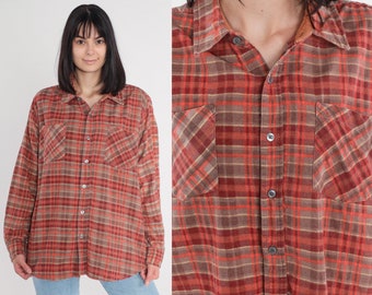 May include: A long-sleeved, button-down flannel shirt in a plaid pattern of red, brown, and tan. The shirt has two chest pockets and a collar. The fabric appears to be soft and slightly worn, suggesting a vintage style.