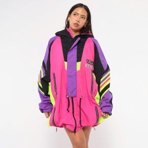 May include: A vibrant, oversized jacket in a retro style. The jacket features a color-blocked design with bright pink, purple, black, and neon green accents. It has a hood, multiple zippers, and a drawstring waist. The jacket has the text "R.P.D. DEMO" on the chest.
