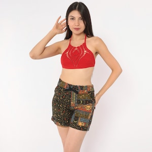 May include: A bright red crochet halter top featuring an intricate openwork pattern and a pair of dark-colored shorts with a multi-patterned patchwork design, including floral and celestial motifs, finished with a black drawstring waistband.