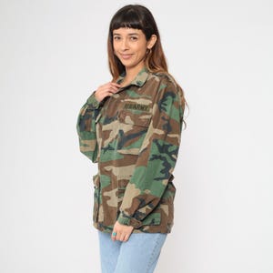 May include: A camouflage jacket with a US Army patch on the left chest. The jacket is made of a cotton blend and has a button-up front.