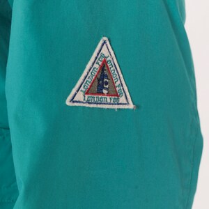 K&ouml;nnte beinhalten: Eine t&uuml;rkisblaue Jacke mit einem wei&szlig;en dreieckigen Patch, auf dem in einer stilisierten Schrift "London Fog" steht.