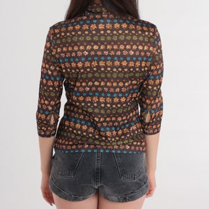 May include: A brown, long-sleeved shirt with a floral pattern in shades of orange, blue, and green. The shirt has a mock neck and a fitted silhouette.
