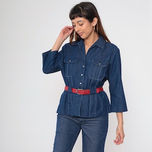 May include: A denim shirt with a red belt. The shirt has a button-down front, two chest pockets, and three-quarter sleeves. The red belt cinches the waist. The model is wearing blue jeans.