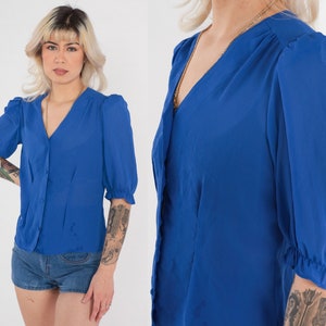 May include: A royal blue, short-sleeved button-up blouse with a V-neckline and puffed sleeves.