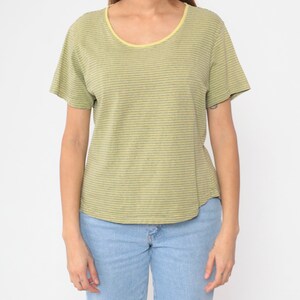 Peut inclure: T-shirt &agrave; rayures vertes et jaunes avec un col rond et des manches courtes. L'encolure est bord&eacute;e de jaune. Le t-shirt est associ&eacute; &agrave; un jean bleu clair.