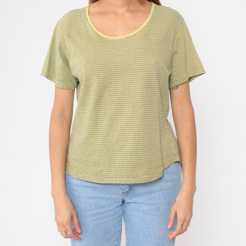 Peut inclure: T-shirt &agrave; rayures vertes et jaunes avec un col rond et des manches courtes. L'encolure est bord&eacute;e de jaune. Le t-shirt est associ&eacute; &agrave; un jean bleu clair.
