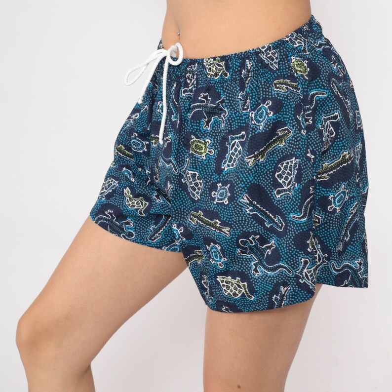 May include: Blue swim shorts with a white drawstring and a pattern of green and white turtles and lizards on a blue background.