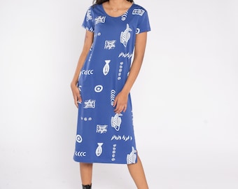 May include: A blue midi dress with a white fish and abstract pattern. The dress has short sleeves and a scoop neckline. The model is wearing black boots. The dress is knee-length.
