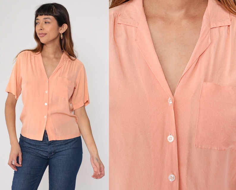 Puede incluir: Camisa melocot&oacute;n de manga corta con cuello y bolsillo en el pecho. La camisa est&aacute; abotonada. La modelo lleva vaqueros azules. La camisa tiene un corte relajado.