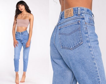 May include: A pair of light blue high-waisted jeans with a faded wash and a straight leg fit. The jeans have a button fly and belt loops. The back pockets have a stitched design. The jeans are made by Jordache.