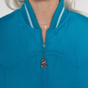 May include: A teal blue bomber jacket with a white and teal striped collar and a zipper with a swan charm.